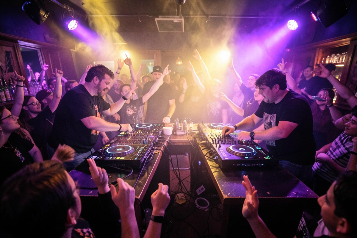 Two DJs playing back-to-back sets to a packed dance floor under purple and gold lights